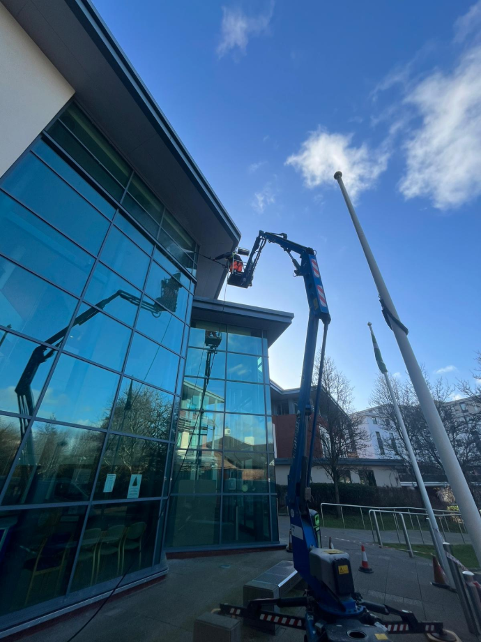 a large glass fronted commercial building being cleaned via a man in a high lift