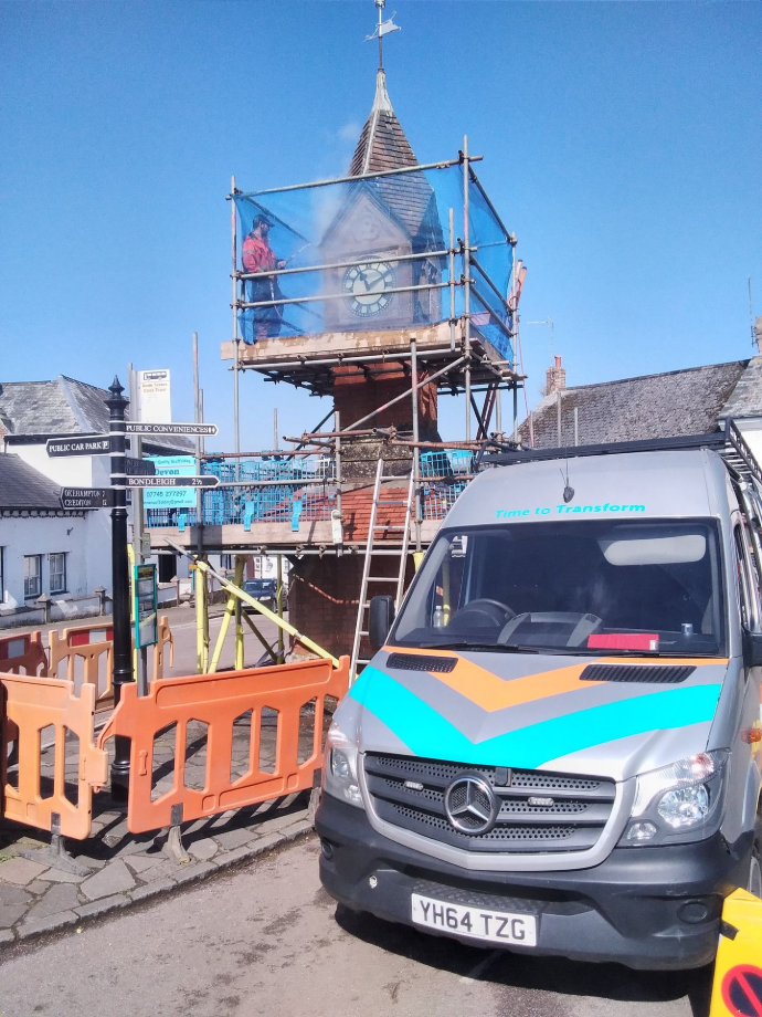 scaffolding around a clock tower with a man steam cleaning the brickwork